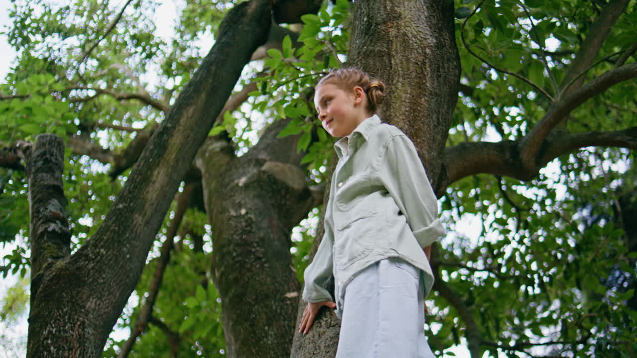 Child girl waving hand climbing tree closeup. Funny kid looking camera posing