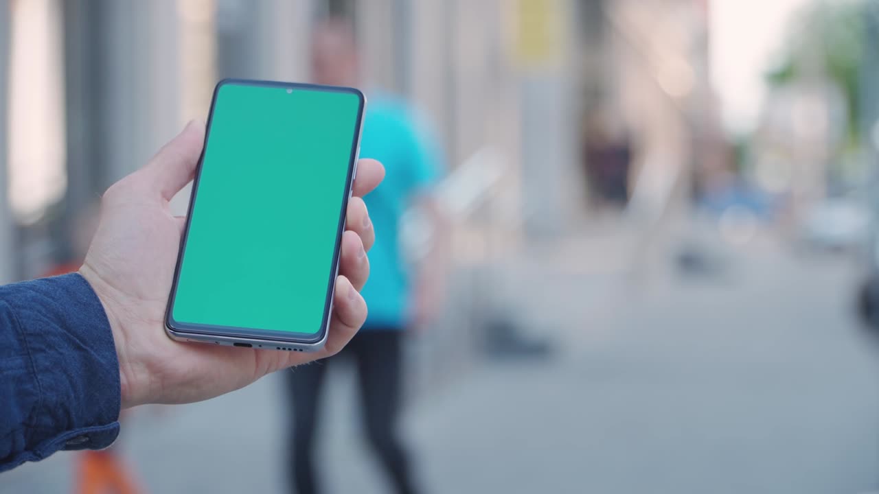 close-up de 4k de la mano de un hombre sosteniendo un teléfono inteligente con pantalla verde en una calle de la ciudad