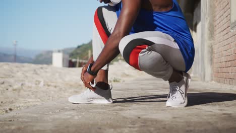 midsection of african american man tying shoelaces during exercise outdoors on beach