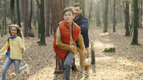 caucasian happy father with his daughter and little son running and playing in the forest