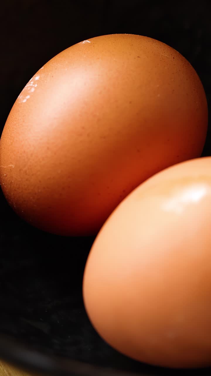 Slow panning close-up of fresh brown chicken eggs in black bowl under soft lighting