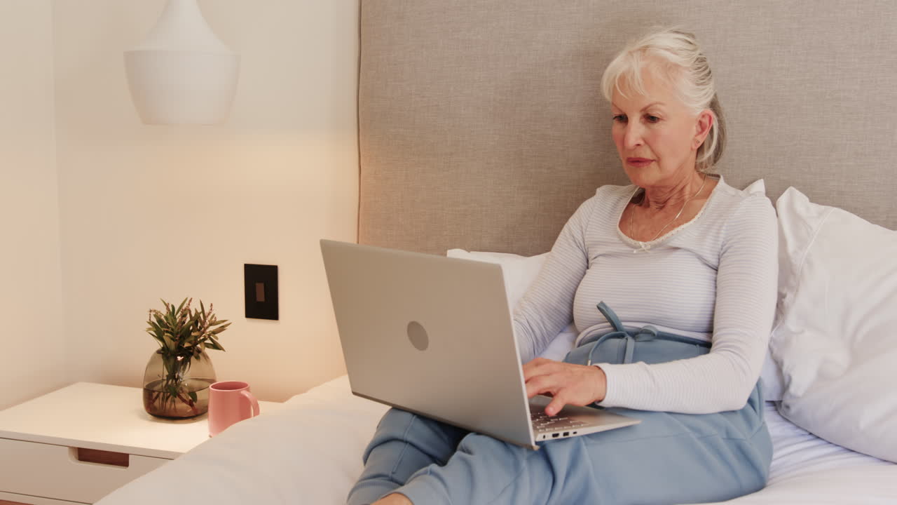 Senior woman using laptop in bed, focusing on work at home