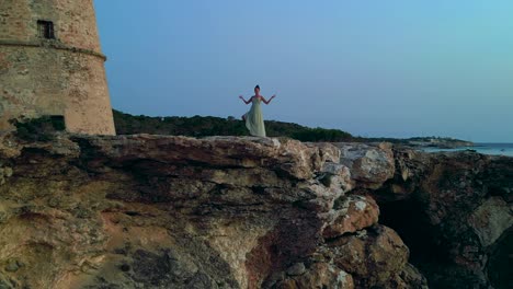 barefoot hippie girl practicing yoga at sunset near torre des carregador, ibiza, spain. speed ramp hyper motion time lapse. nice aerial view flight overflight flyover drone