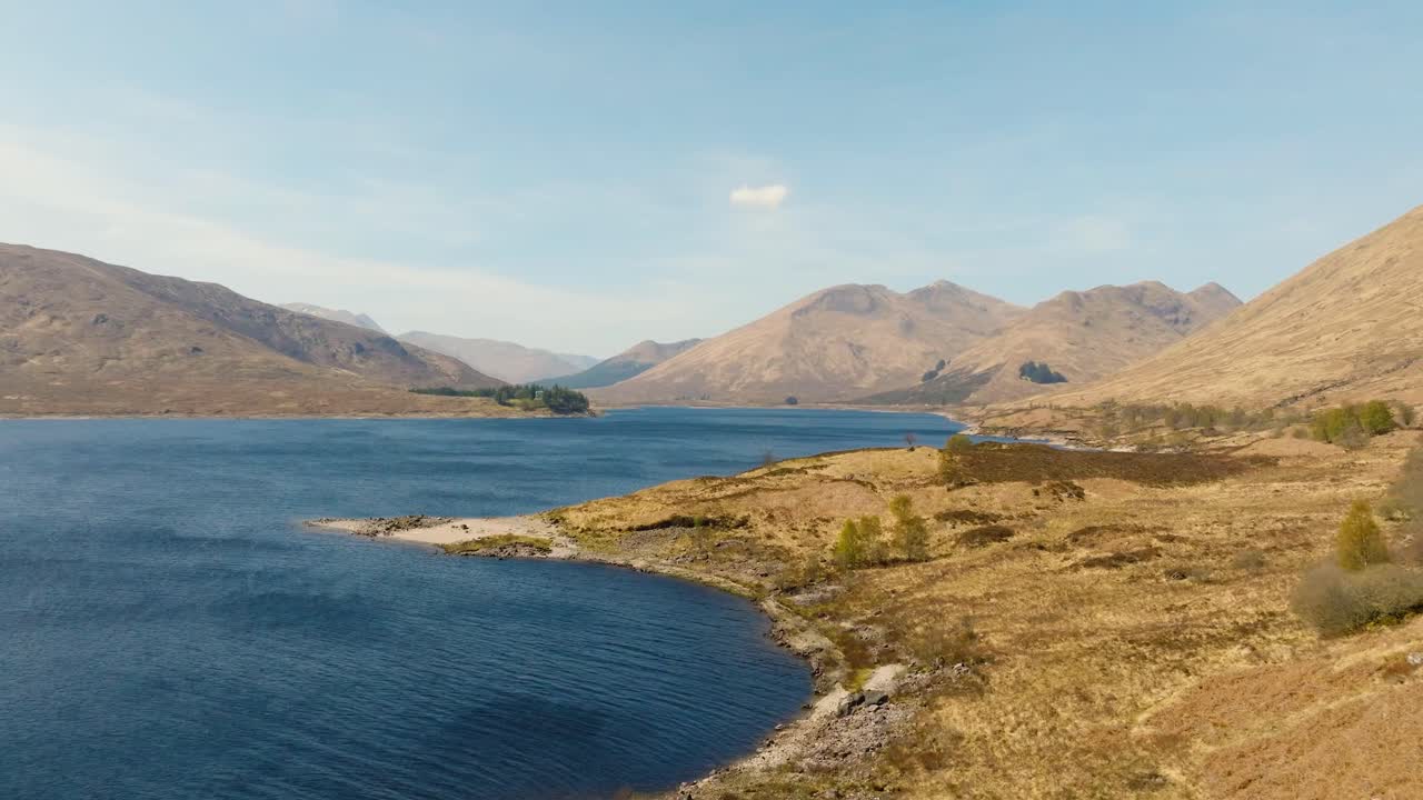 Aerial drone footage of a scenic lake surrounded by rugged Scottish landscape. Panoramic views of calm waters, rolling hills, and untouched wilderness, capturing the raw beauty of the Highlands