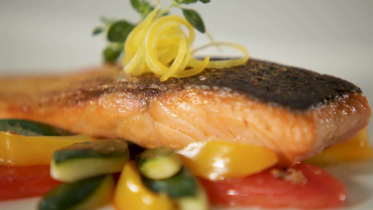 Close-up shot of a perfectly cooked salmon fillet served with colorful vegetables and lemon zest