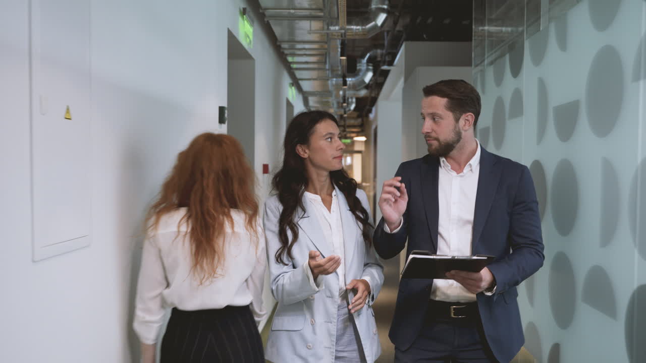 A young businessman and a young businesswoman walk through the corridors of an office building discussing company matters.