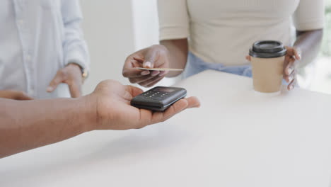 midsection of african american woman making contactless card payment for coffee in cafe, slow motion