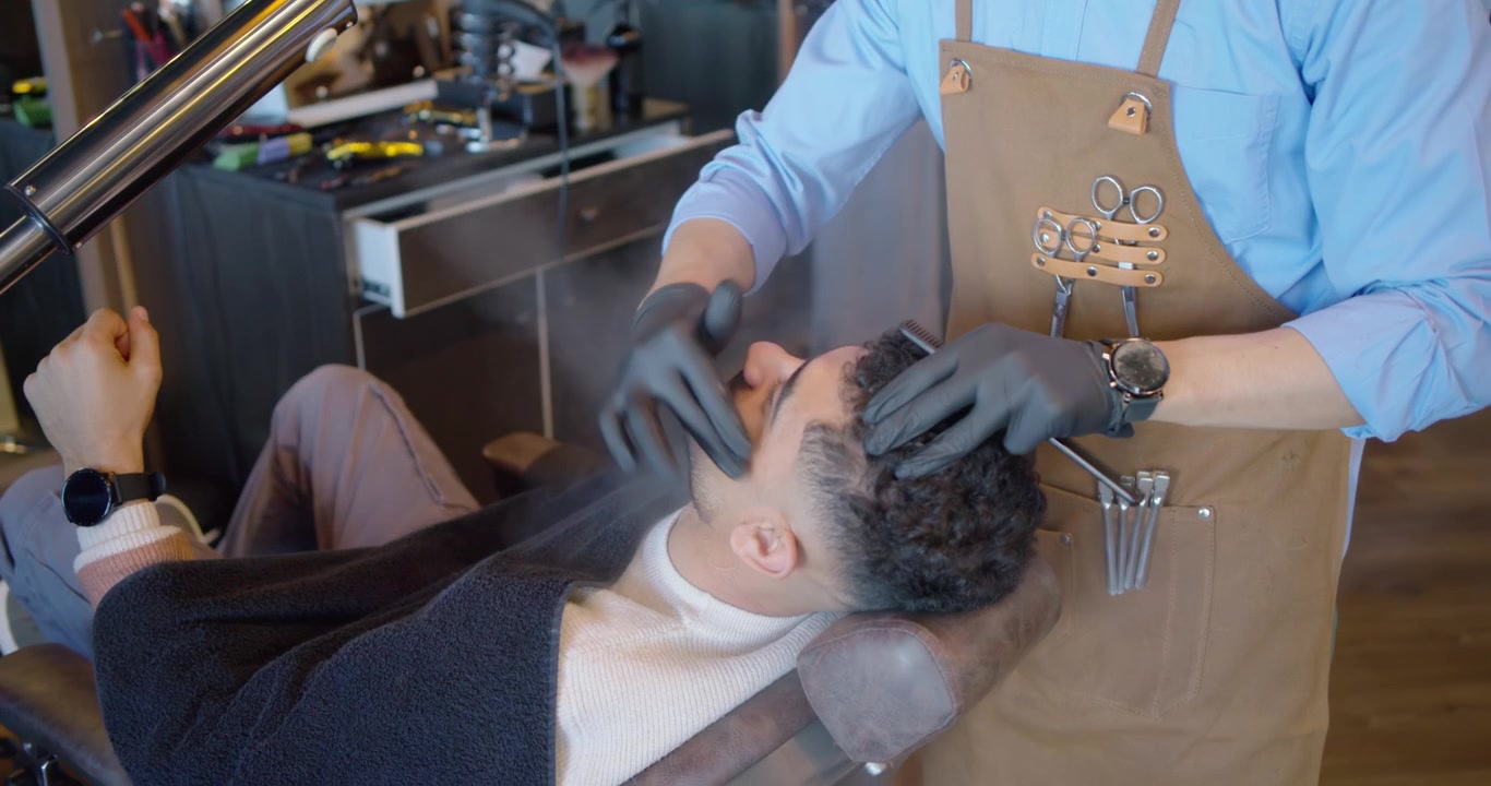 Mandlig kunde læner sig tilbage, mens frisøren aktiverer en damper, masserer og reder krøller til styling.
