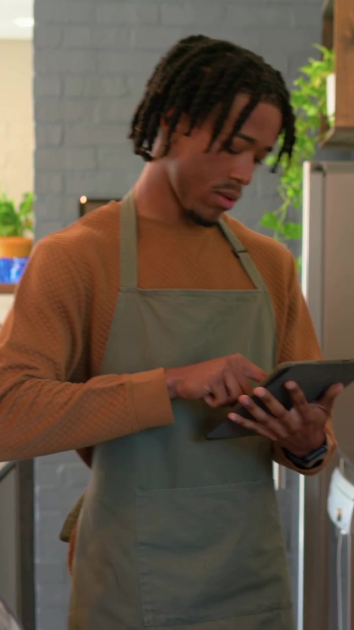 Vertical video: Woman picking cups at counter, barista in green apron making espresso, using tablet