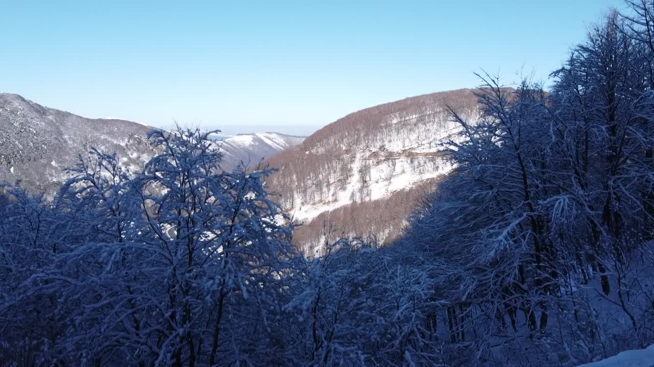 눈 덮인 산, 계곡을 가로지르는 도로, 배경에는 바다가 보이는 드론 이미지