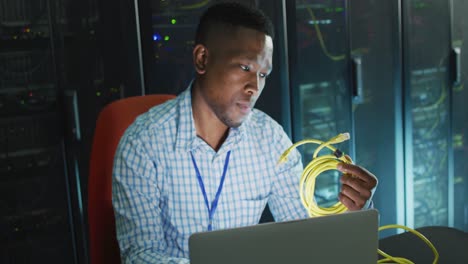 African-american-male-computer-technician-laptop-working-in-business-server-room