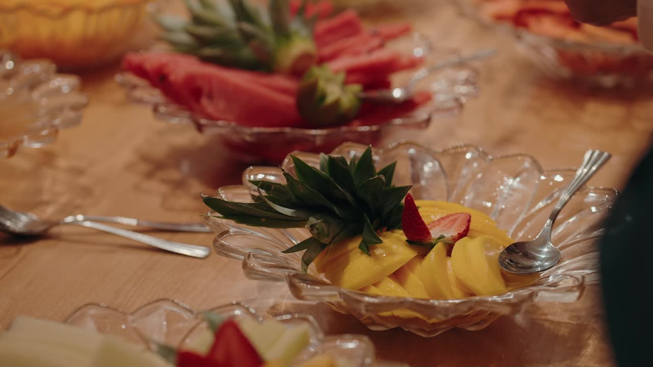fork lifts strawberry from mango fruit bowl on wood table