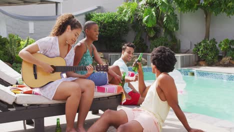 mujer biracial feliz tocando la guitarra y cantando con un grupo de amigos diversos en una fiesta en la piscina