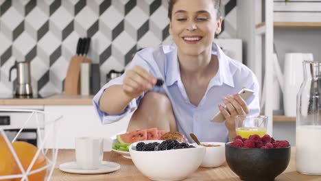 Mujer-Joven-Usando-Un-Teléfono-Móvil-Durante-El-Desayuno-En-La-Cocina.