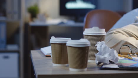 Vista-De-Cerca-Del-Trabajador-De-Oficina-Durmiendo-En-El-Escritorio-Lleno-De-Tazas-De-Café-Vacías-En-La-Noche