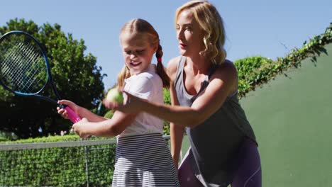 caucasian mother teaching her daughter to play tennis at tennis court on a bright sunny day
