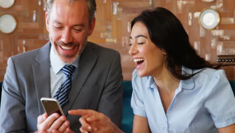 Woman-and-businessman-smiling-while-using-mobile-phone