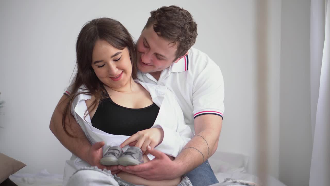 Joven embarazada con su esposo esperando un bebé. La joven familia espera la llegada de un nuevo miembro. Mujer embarazada feliz con gran barriga descansando en casa. Joven futura madre acaricia su vientre