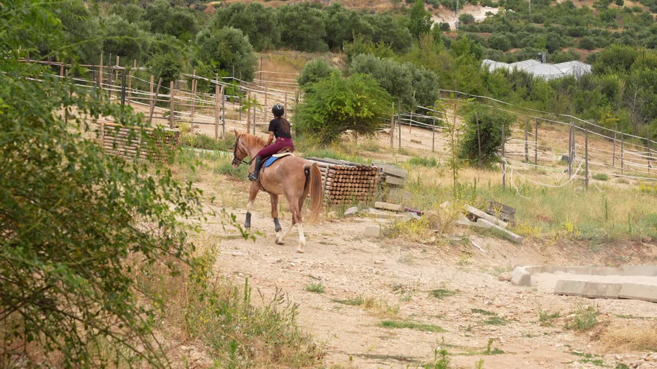 Female horse rider leaves riding track heading back to stable in equestrian center