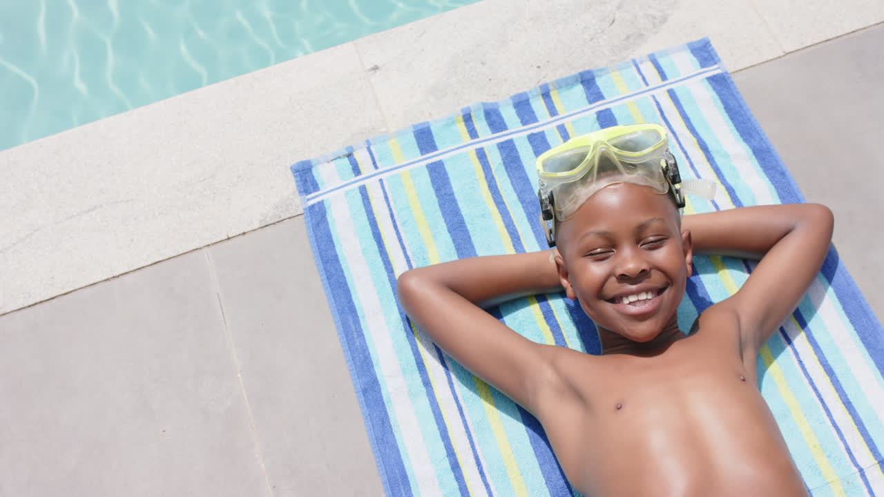 High angle of happy african american boy in goggles sunbathing by pool, copy space, slow motion
