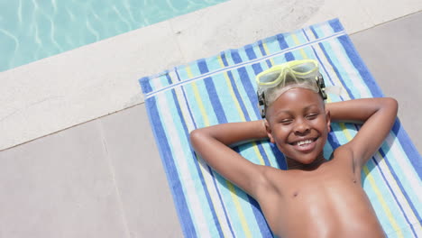 Alto-ángulo-De-Feliz-Niño-Afroamericano-Con-Gafas-Tomando-El-Sol-Junto-A-La-Piscina,-Espacio-Para-Copiar,-Cámara-Lenta