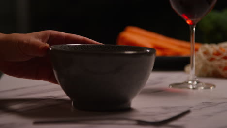 close up of woman at home in kitchen preparing healthy vegetarian or vegan meal pouring sauce onto bowl of tabbouleh salad with glass of wine 2