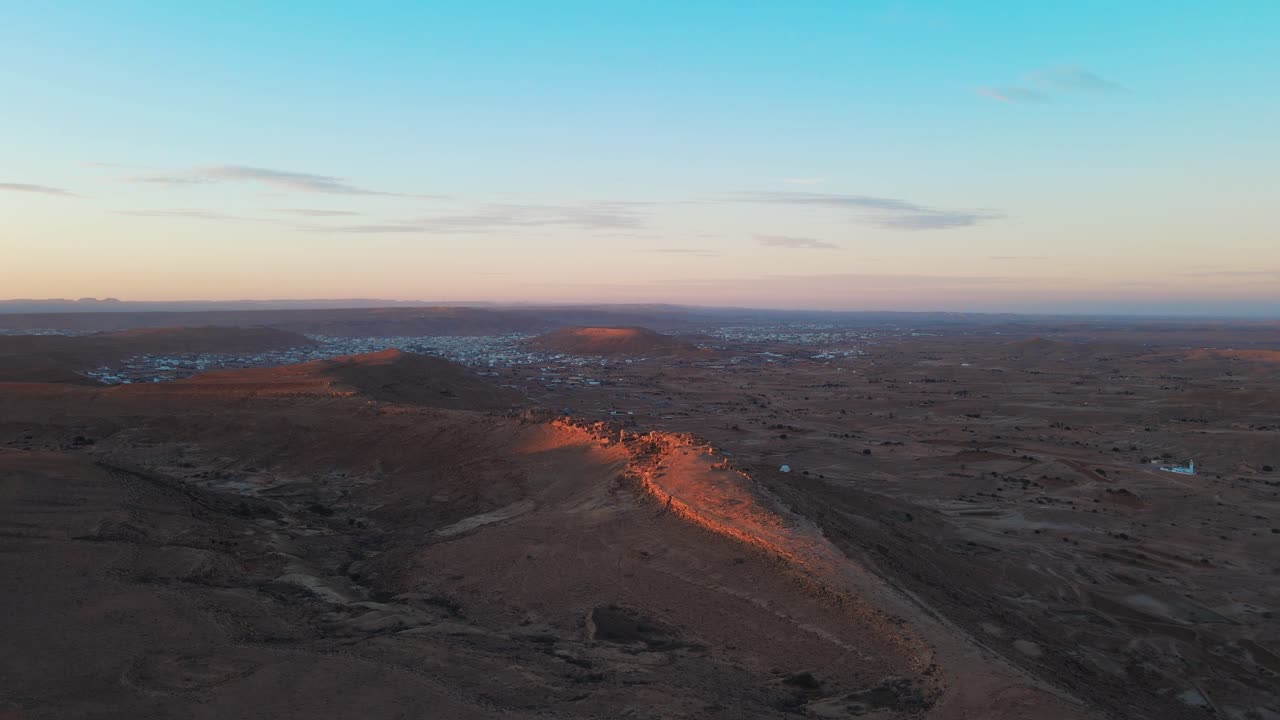 Aerial view of Ksar Jarrat, Tunisia at sunset. Desert landscape with town in distance.