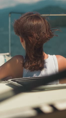 relaxed woman with messy hair looks in distance leaning out of yacht hatch on windy day. lady contemplates seascape from boat on summer vacation