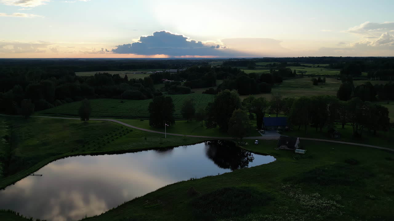 el lapso de tiempo de una puesta de sol, el sol se esconde detrás de la nube, con campos verdes y árboles y un pequeño lago cerca de una casa de una sola familia, copiar el espacio