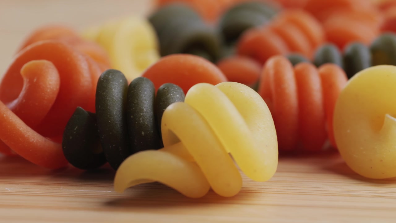 Nærbilde av ukokt trefarget fusilli-pasta på en treoverflate