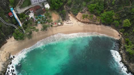 Above-the-blue,-bird's-eye-view-of-Coral-beach's-crystal-clear-at-Puerto-Escondido,-Oaxaca,-Mexico