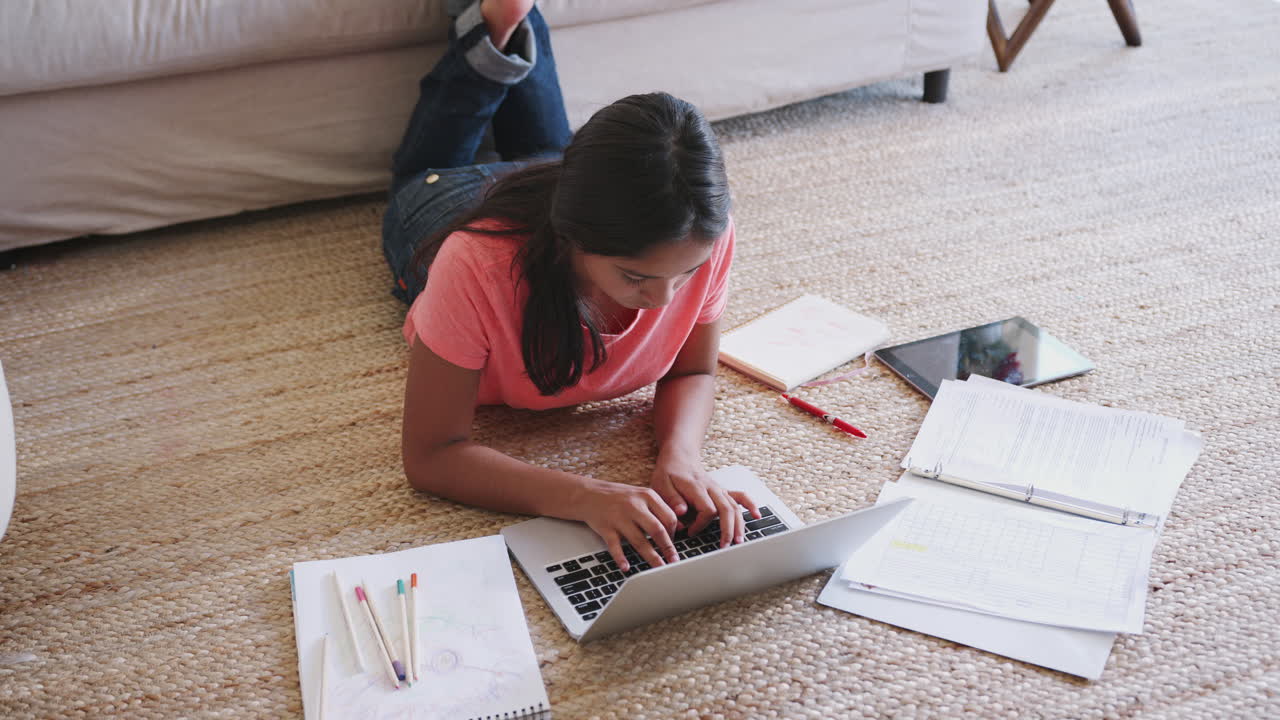 Teenage girl lying on the floor doing her homework using a laptop computer, elevated view, close up