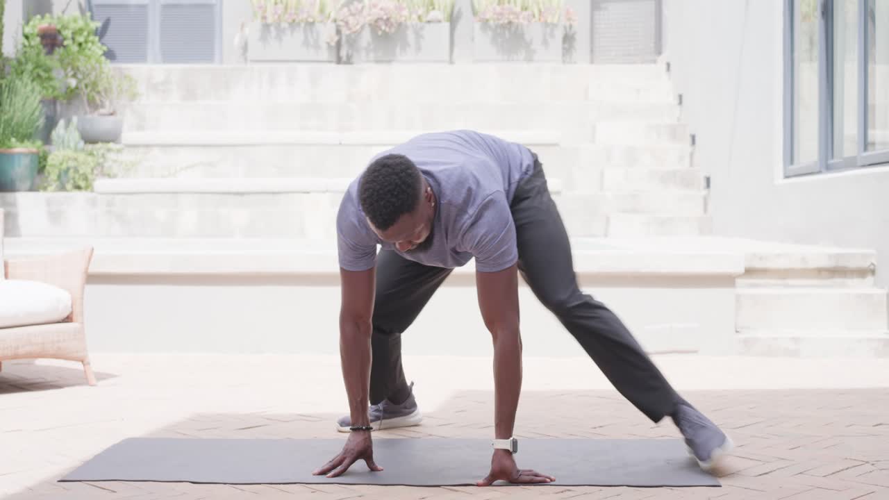 Man wearing t-shirt kneeling on mat on brick patio warming up before workout reaching shoe