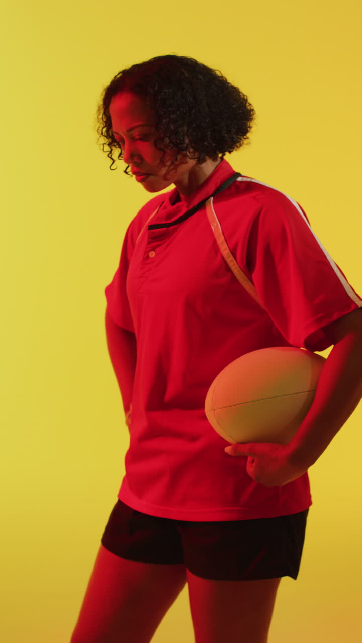 video vertical de una jugadora de rugby afroamericana con una pelota de rugby sobre una iluminación rosa de neón