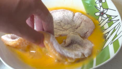 male hands turning flour coated schnitzel in egg wash in slow motion