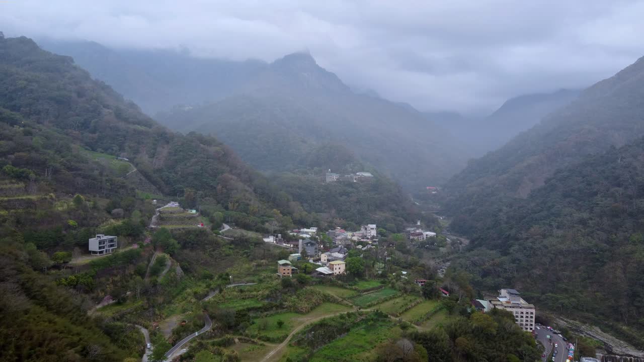pueblo de montaña nebuloso enclavado en un valle exuberante, día nublado, vista aérea