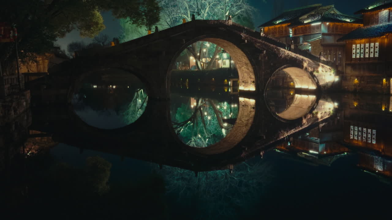 Bridge in Wuzhen, China, reflecting in tranquil water at night with glowing lights