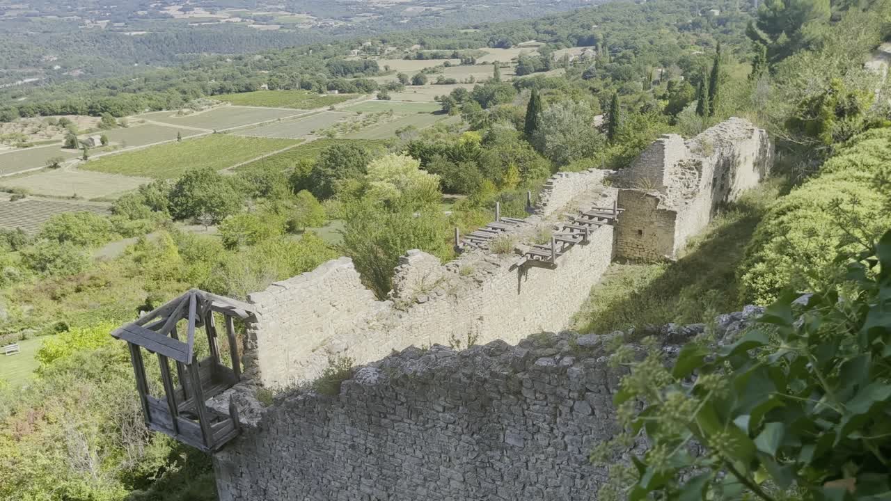 Vecchia rovina in pietra con muro e vegetazione in Francia di fronte a un ampio paesaggio forestale con boschi e campi in lontananza fino all'orizzonte con bel tempo