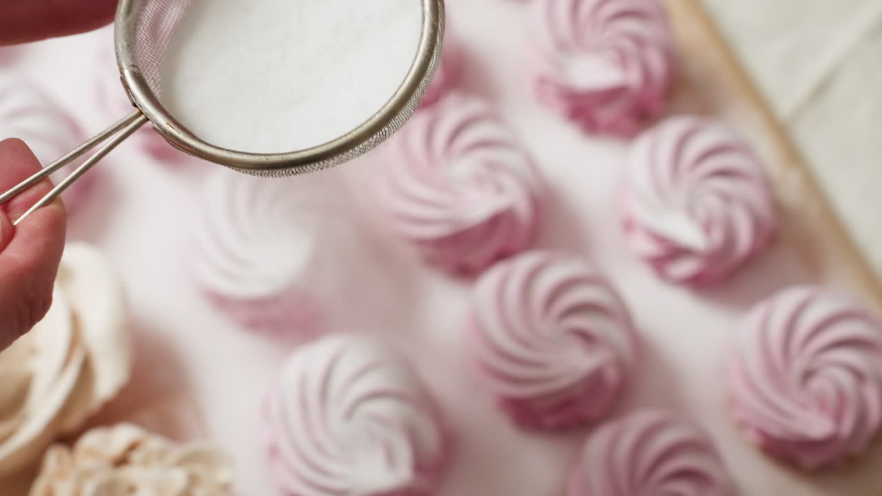 Close up of baker holding fine mesh sifter and carefully sprinkling sugar over neatly arranged swirl cupcakes in perfect rows on parchment paper, showcasing precision
