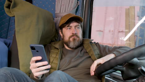 Worker Wearing Cap And Vest Tumbado Lying On Truck Seat While Using Smartphone 1