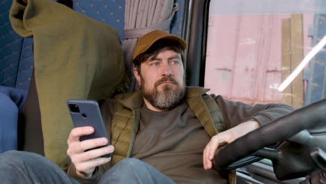 worker wearing cap and vest tumbado lying on truck seat while using smartphone 1