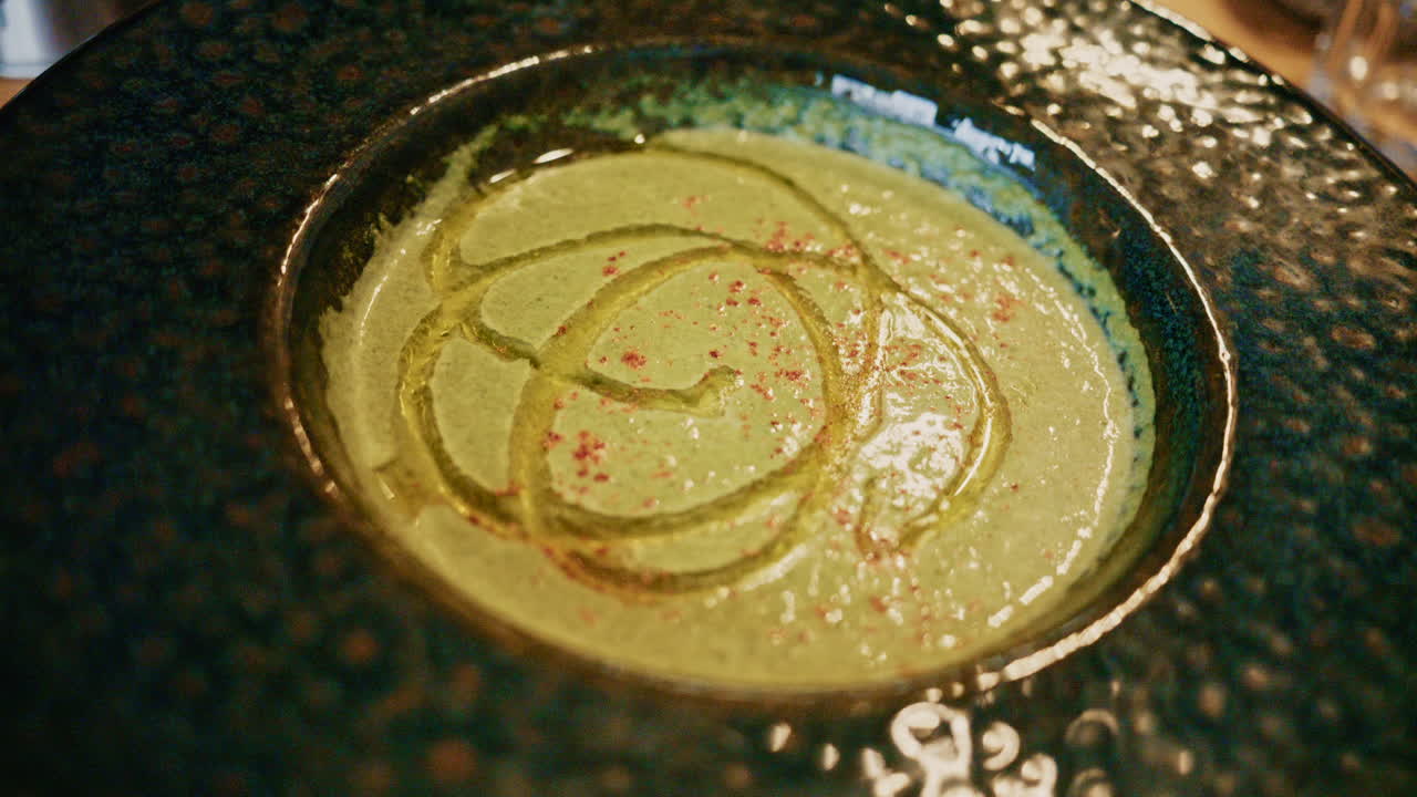 Vista superior de uma sopa verde cremosa decorada com óleo e especiarias, servida em uma tigela de cerâmica sobre uma mesa de madeira