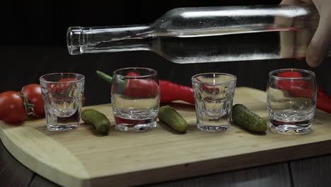 pour vodka into shot glasses placed on a wooden board