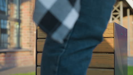 close up of modern wooden slat trash bin in urban area with person walking away after discarding item, sunlight casting soft shadow over clean surface with building and grass in background