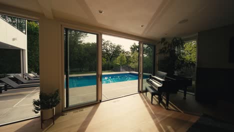 inside the living room of a large luxury home looking out to a large pool through open sliding doors during sunrise with water reflections visible on the ceiling