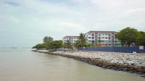 Vista-Diurna-De-Costas-Rocosas-A-Lo-Largo-De-Un-Mar-Tropical,-Con-Casas-En-Construcción-Al-Fondo