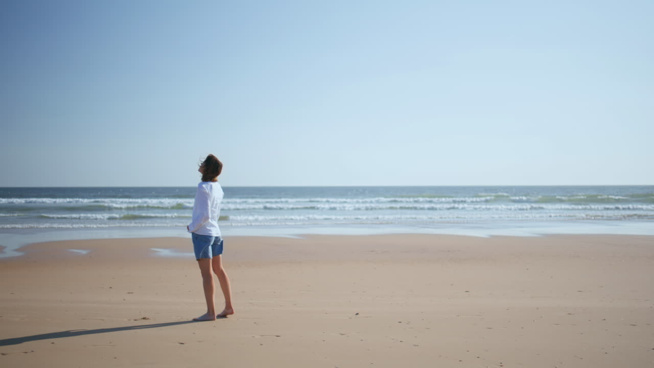 Woman strolling serene beach in summer sunlight. Lady enjoying rest near ocean