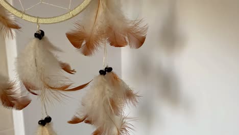 hanging dream catcher adorned with feathers in a white background corner room blowing in the breeze