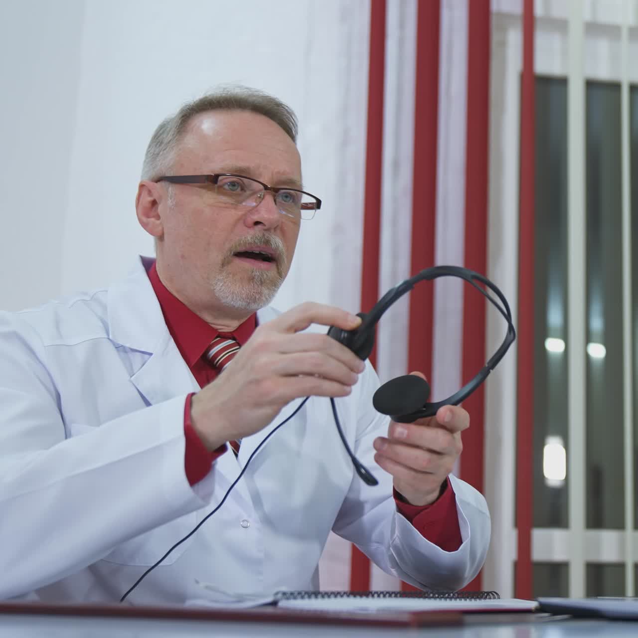 Happy satisfied mature doctor is working with patient via phone. Looking at phone in modern clinic office. Closeup