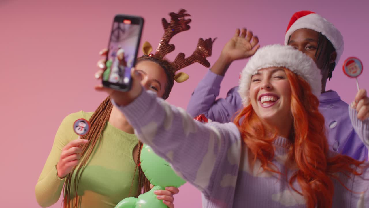 Foto Studio Teman Gen Z Menari dan Berpose Swafoto di Pesta Natal Mengenakan Topi Santa dan Tanduk Rusa 2